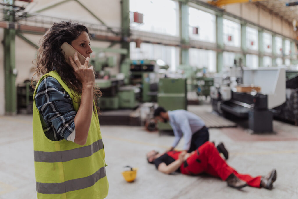 A woman is calling ambulance for her colleague after accident in factory. First aid support on workplace concept.